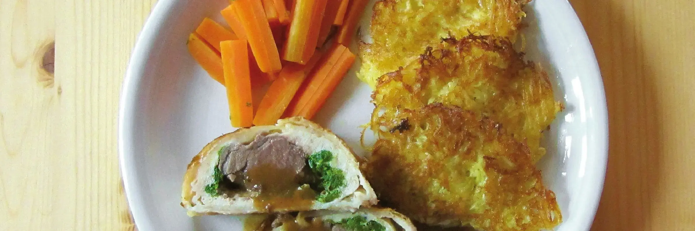 Ein Teller angerichtet mit Rehrücken im Blätterteig, Kartoffelpuffer und Möhren