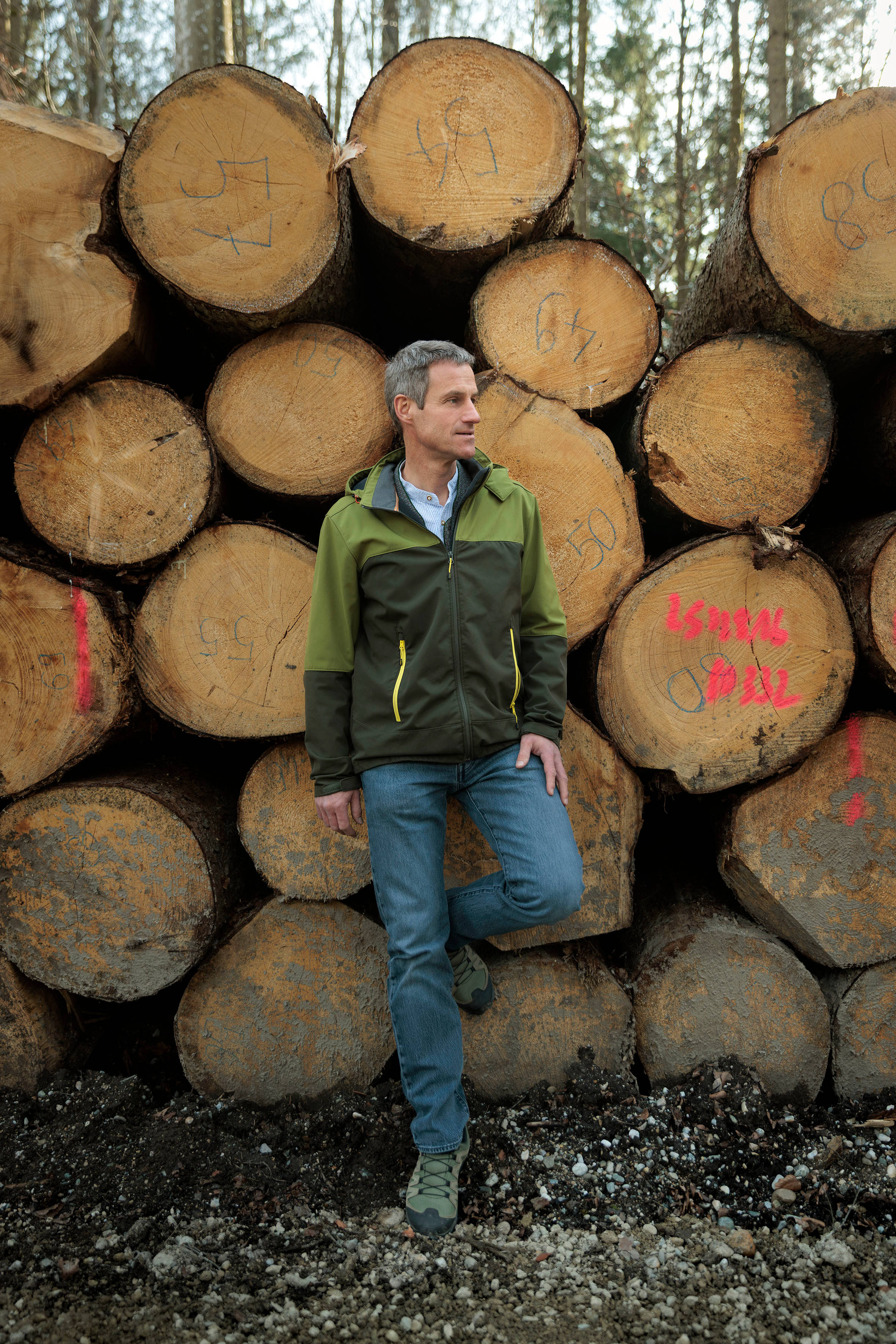 Förster steht vor Holzpolter mit grüner Jacke