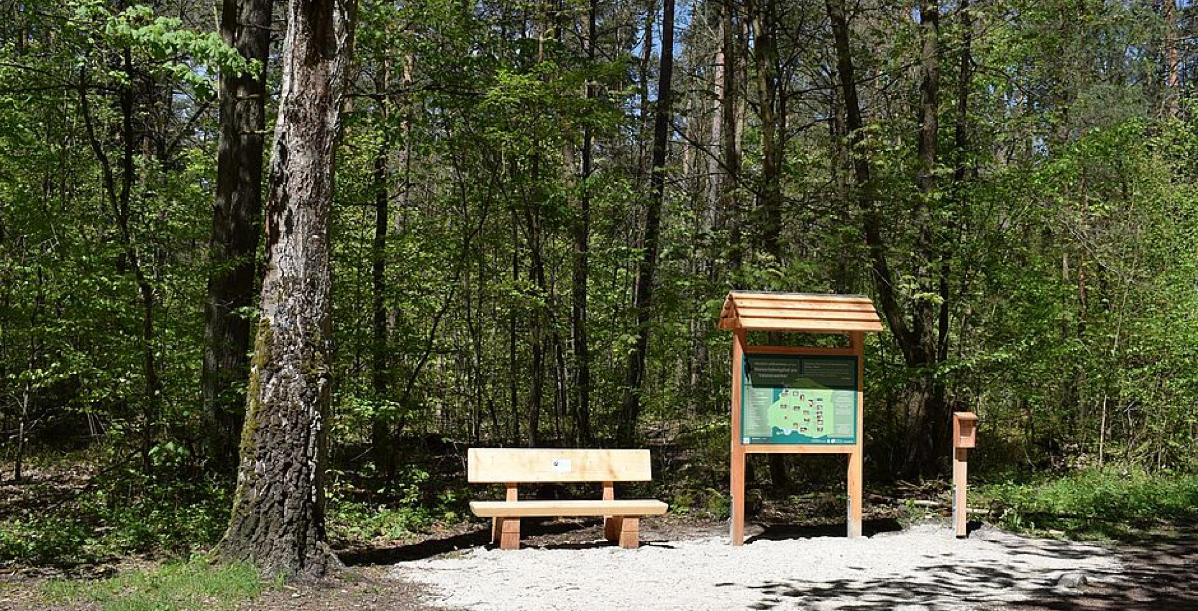 Infotafel steht neben Bank im Wald