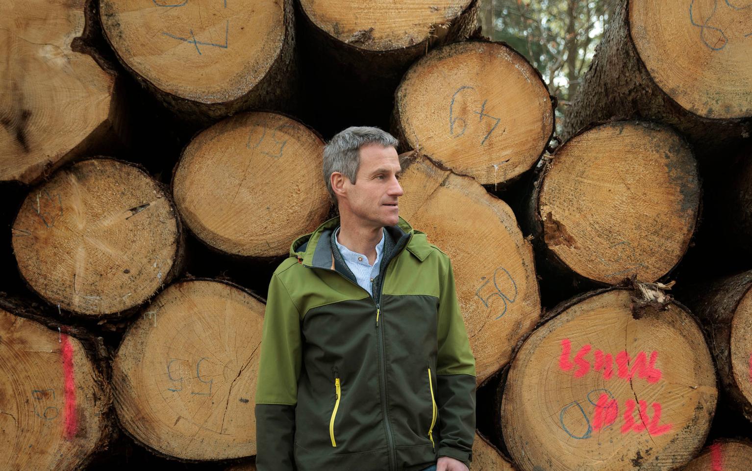 Förster steht vor Holzpolter mit grüner Jacke