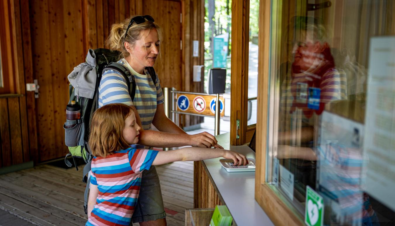 Eine Frau und ein Kind kaufen Tickets für den Baumwipfelpfad Steigerwald