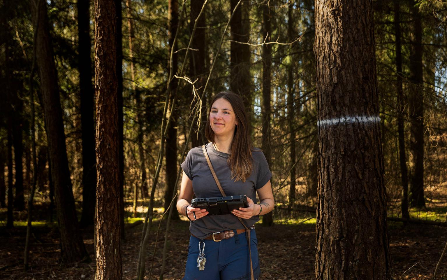 Försterin steht im Wald mit Tablet und Hund