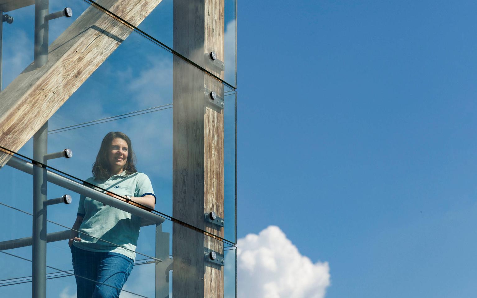 Frau lehnt in glasigem Treppenhaus an Geländer