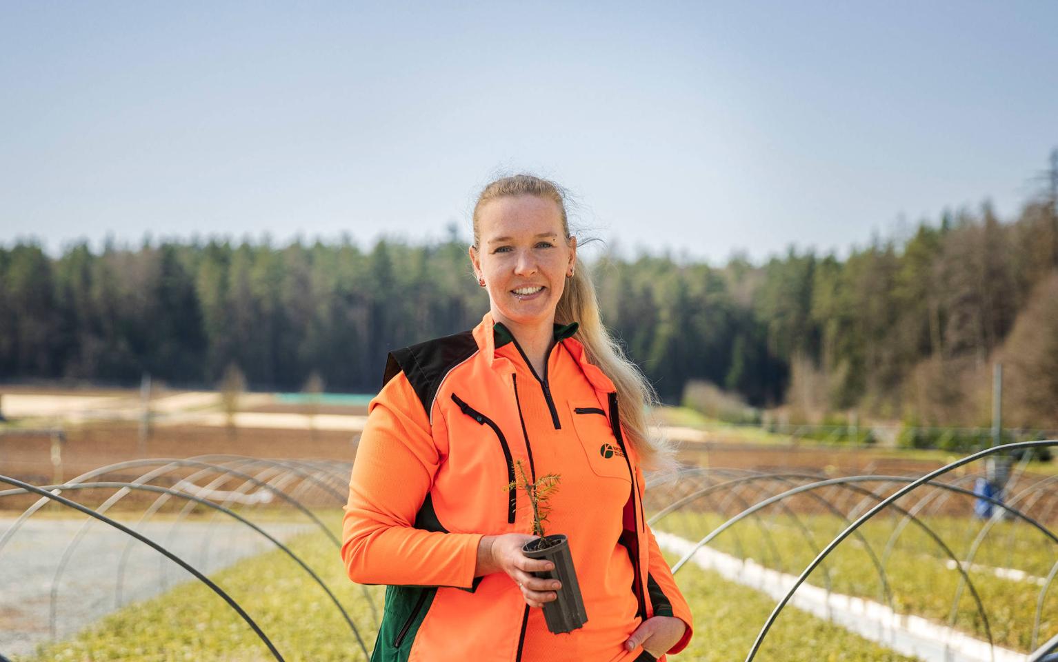 Frau steht in Pflanzgarten zwischen jungen Baumreihen